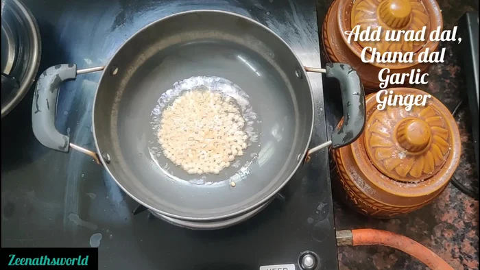 Add 1 tablespoon urad dal, 1 tablespoon peanuts, and 4 peeled garlic cloves. Stir-fry.