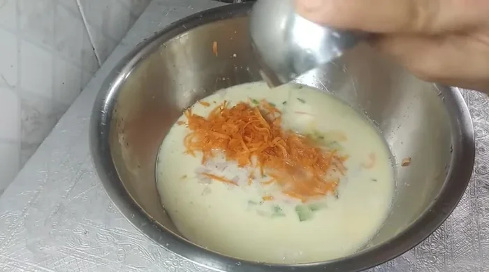 Add capsicum, onion, grated carrot, lemon juice, salt, asafoetida, and cumin to the batter.