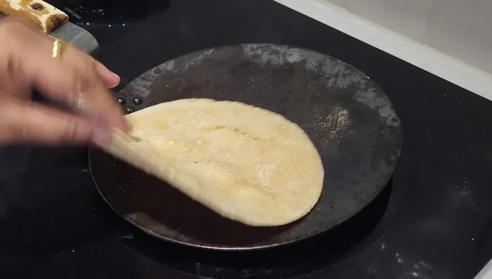 Place a roti on the hot pan. Cook for a short time on one side until you see it begin to dry and brown slightly.