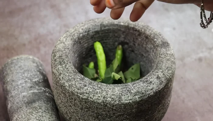 Add 7-8 garlic cloves, 3 green chilies, and 1 sprig of curry leaves to the mixture and grind coarsely.